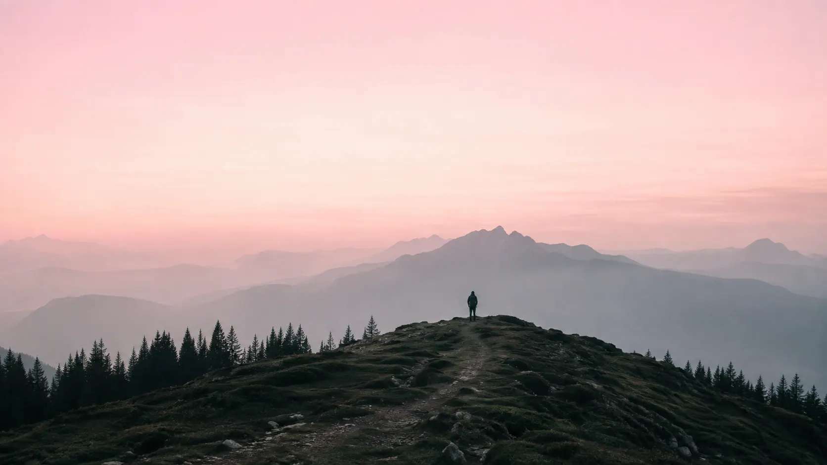 A tiny hiker at the top of a ridge, facing a wide pink horizon of mountains.