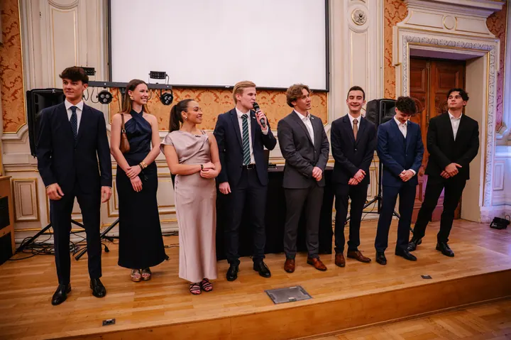 A team in evening dress on a stage, one of them speaking into a microphone.